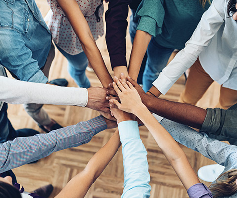A dozen people putting their hands together in a circle