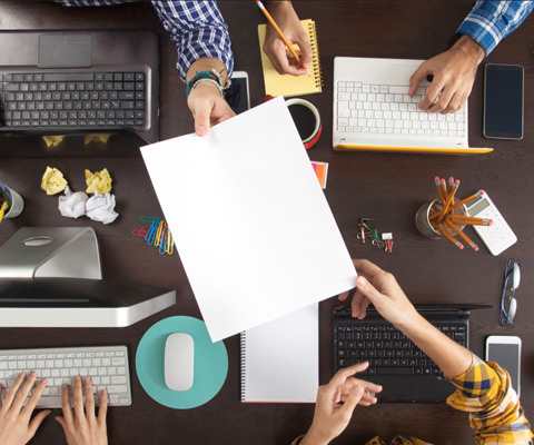Top view of four people working at a dark brown wooden table on computers
