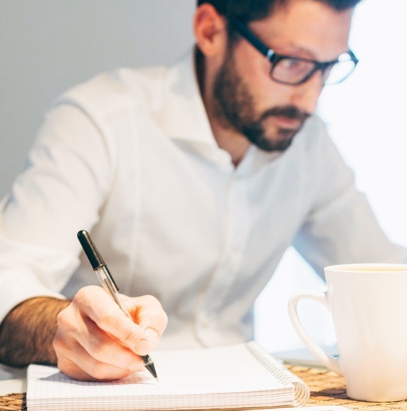 Man in glasses with white shirt writing on graph paper with white coffee mug