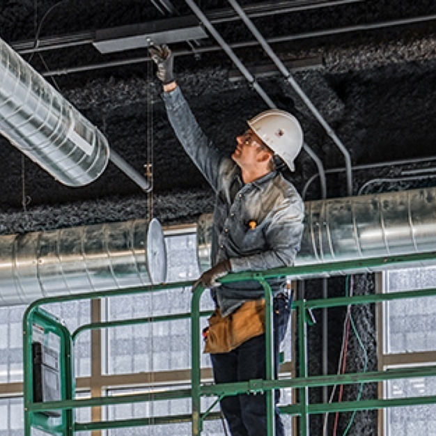 Building inspector on a step ladder looking at the ceiling in an industrial building