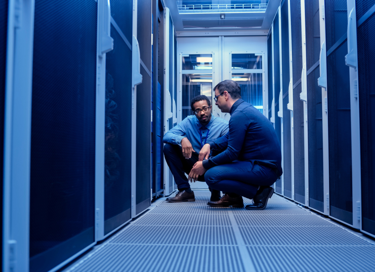 Two men kneeling down on the floor talking in a data center