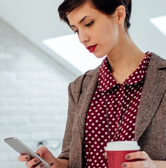 Woman looking at phone with red poka dot shirt and coffee in hand