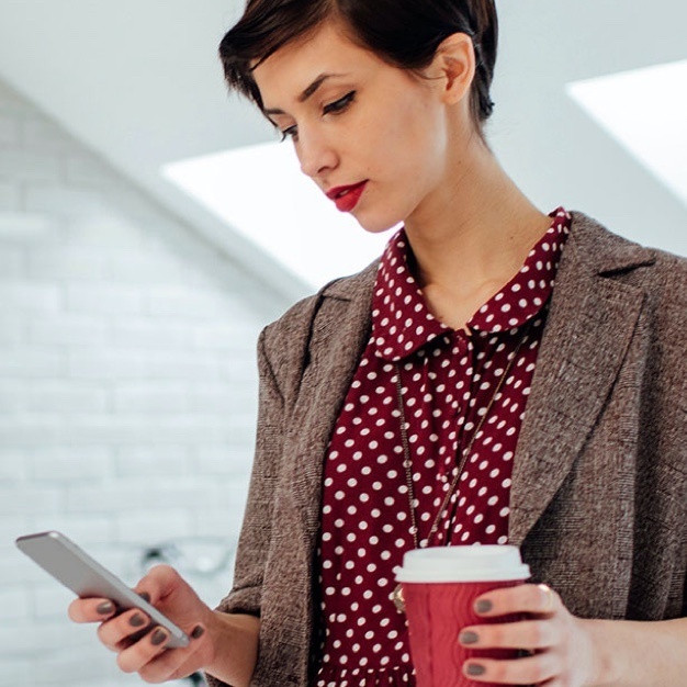 Woman looking at phone with red poka dot shirt and coffee in hand