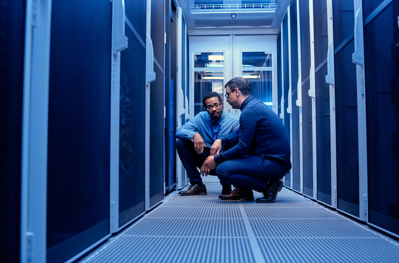 Two men kneeling down on the floor talking in a data center